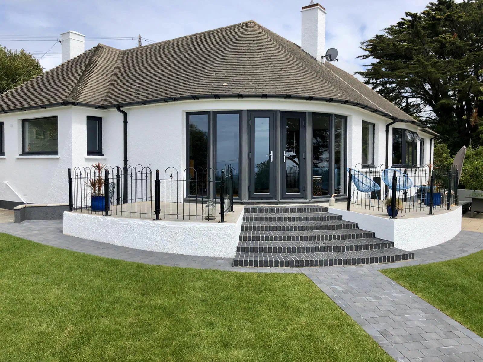 The rear of a white rendered bungalow with dark grey French doors and windows opening onto a raised terrace