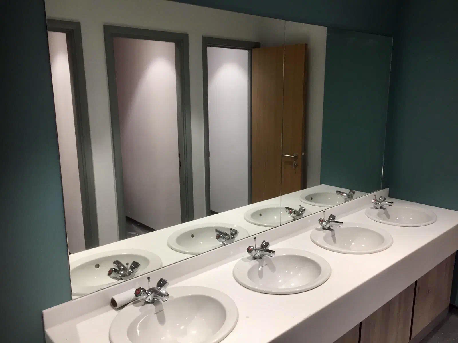 A full-width mirror above a row of four washroom basins